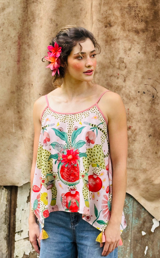 Woman wearing a colorful floral and fruit patterned top against a textured wall.