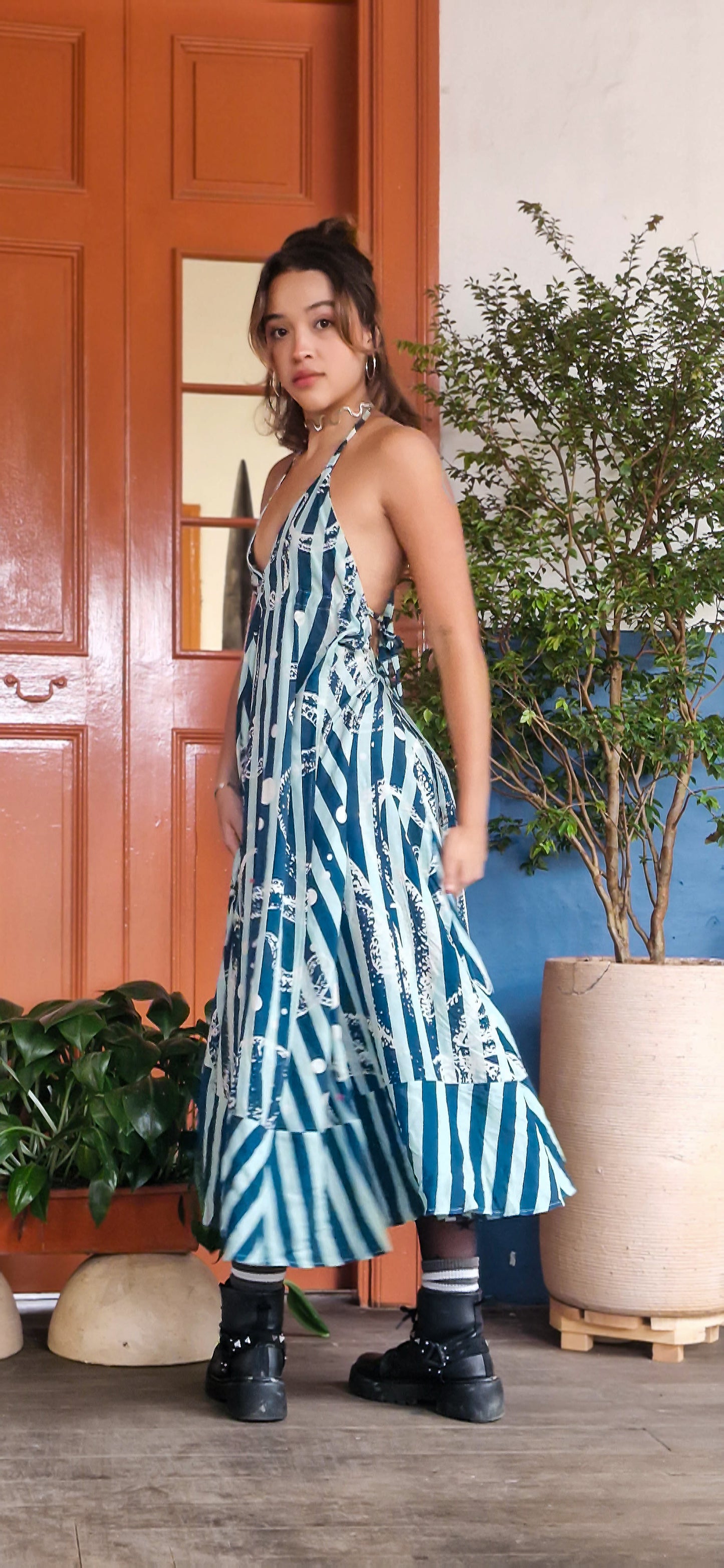 Woman in a blue and white patterned dress standing in front of a door with plants.