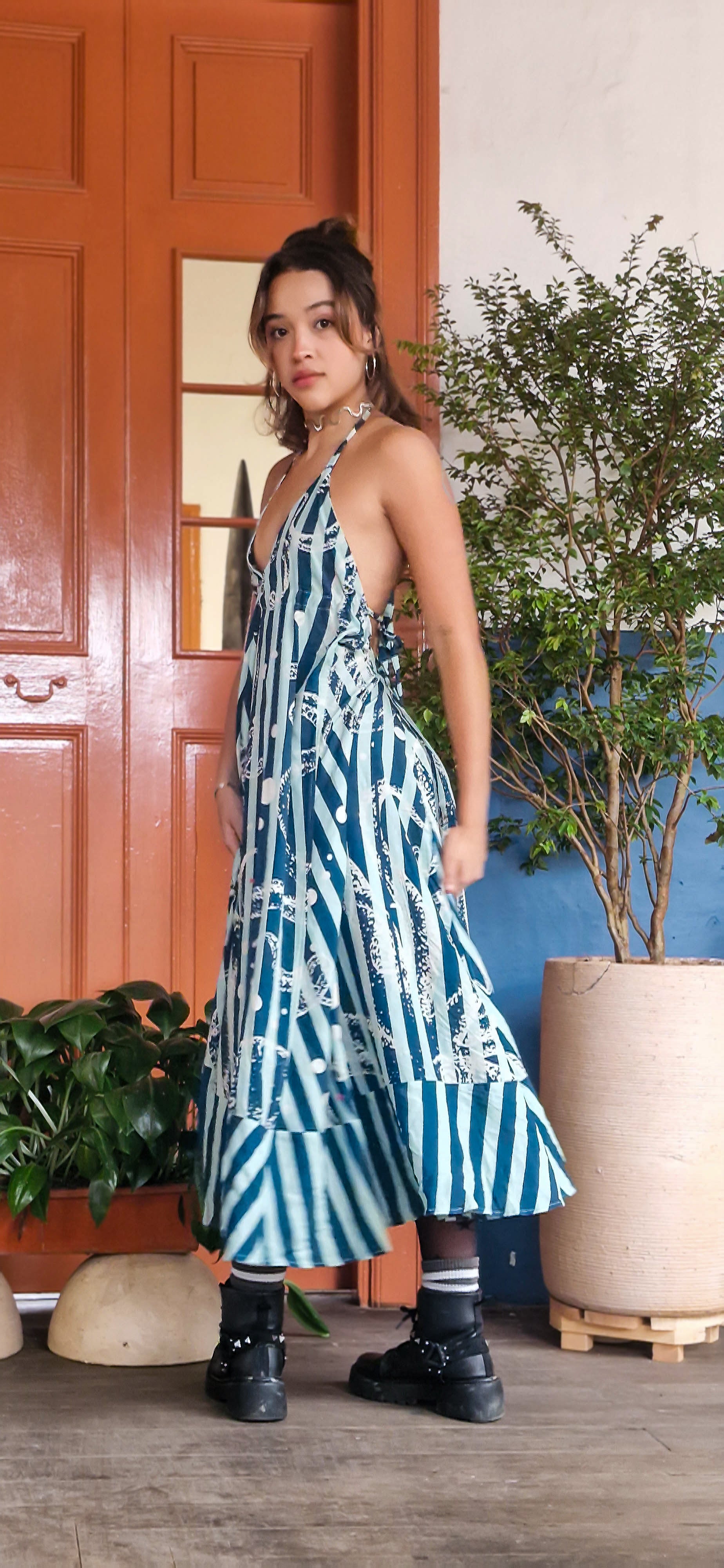 Woman in a blue and white patterned dress standing in front of a door with plants.